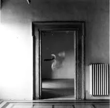Black-and-white photograph of a spectral figure beyond a doorway